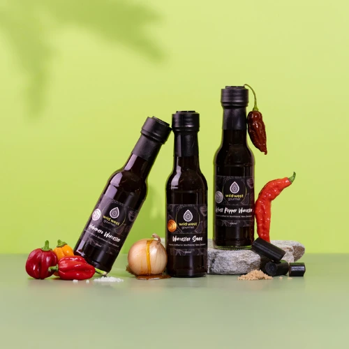 Three bottles of Worcester Sauce, with different chillies surrounding them, and with a crisp green background
